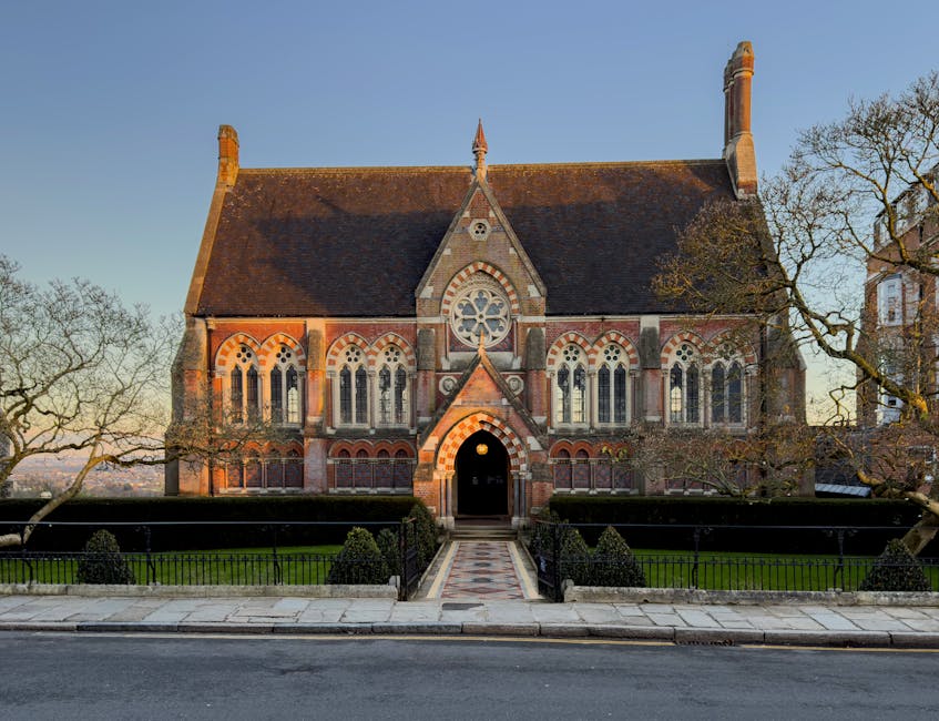 A close-up view of a historic red brick building featuring a prominent bay window with leaded glass panes set in an ornate stone frame. The building's facade shows a stepped, decorative parapet at the